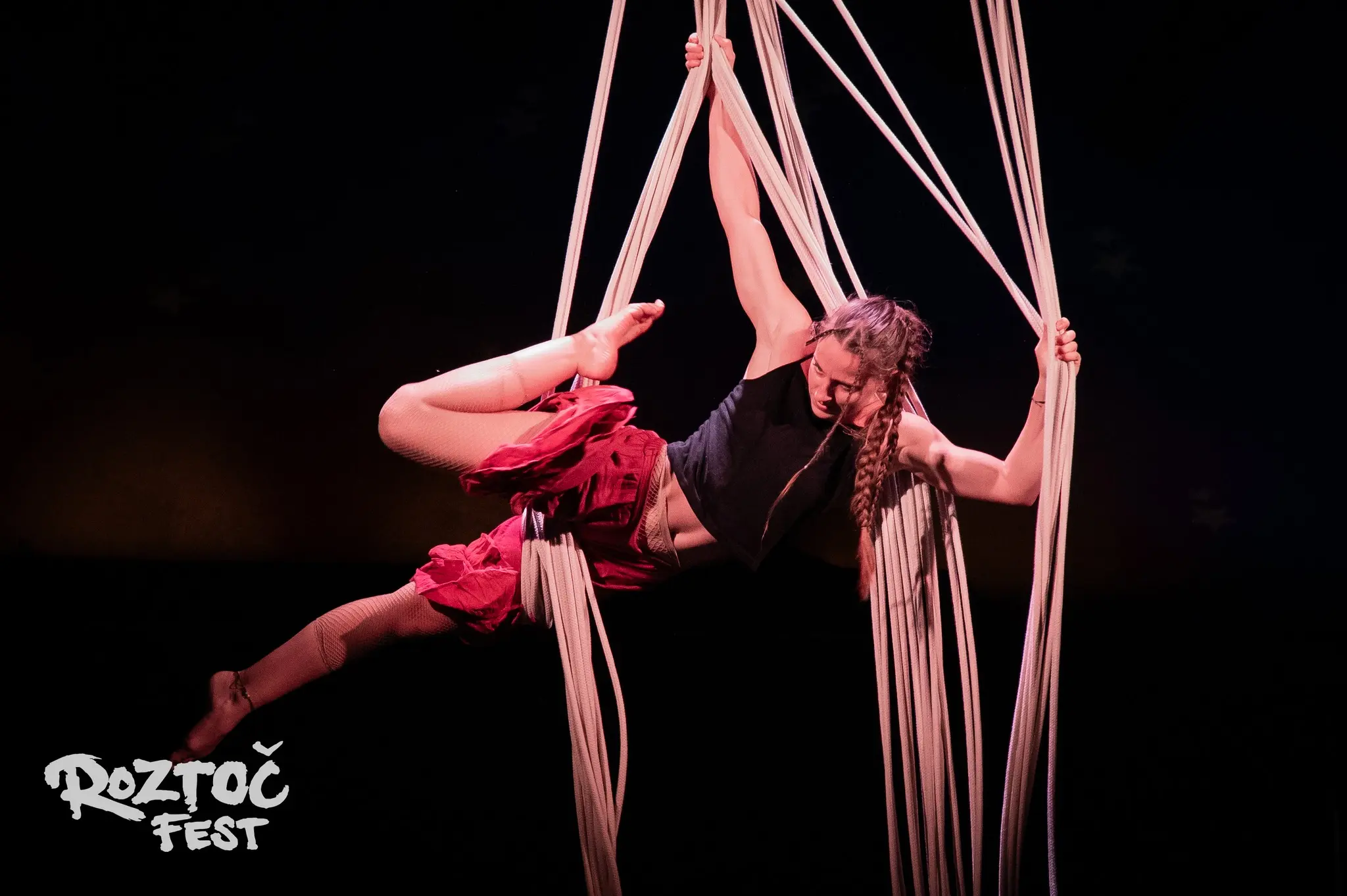Klaudia Bawer wykonująca akrobacje aerial na białej szarfie zawieszonej na drzewie w lesie. Profesjonalny pokaz plenerowy.