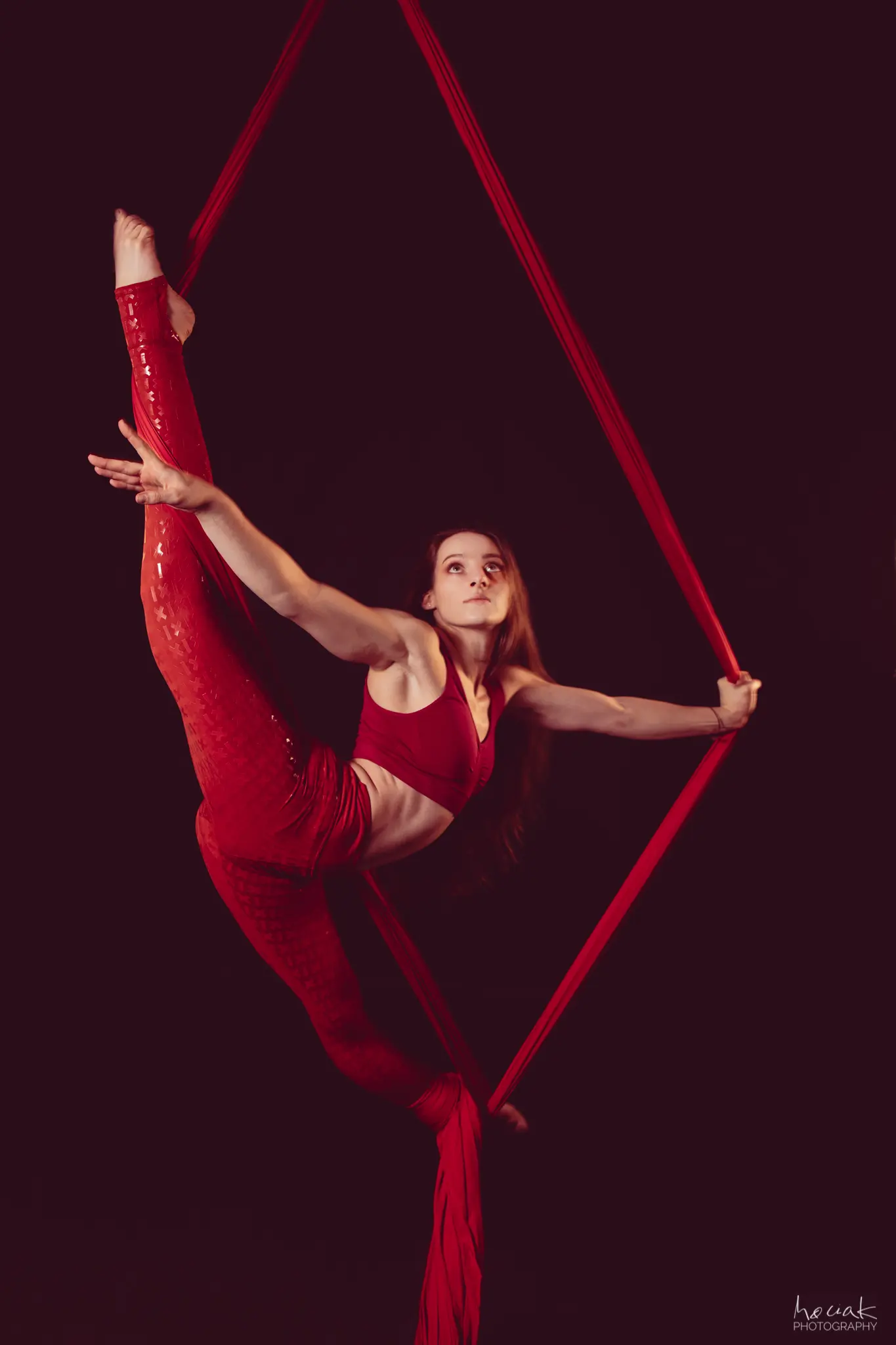 Artystka Klaudia Bawer w pełnym szpagacie pionowym na czerwonej szarfie wertykalnej, profesjonalne ujęcie studyjne na czarnym tle.